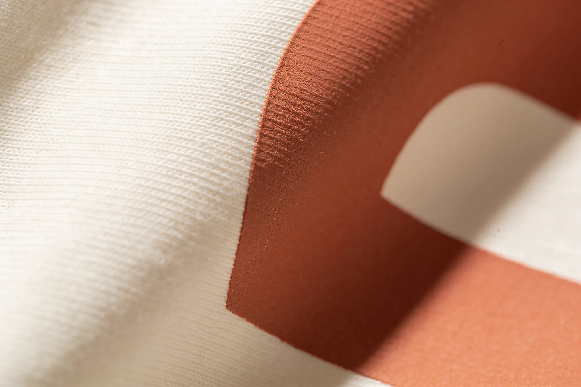 Extreme close up of a clay coloured screen print sitting on the surface of a cream cotton sweatshirt, showing the ink texture against the knit